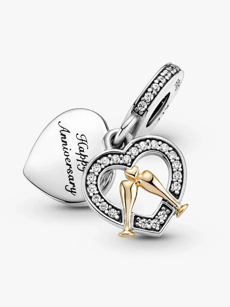 Charm de corazón en ángulo picado sobre fondo blanco, mostrando el grabado y las copas de oro.