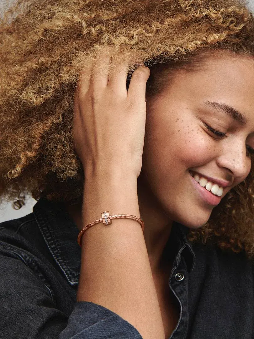 Close-up van armband met separator charm om de pols, lachend model met krullend haar, wazige achtergrond.