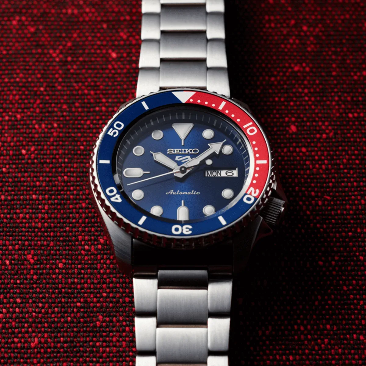 Reloj visto frontalmente sobre fondo de tela texturizada en color rojo.