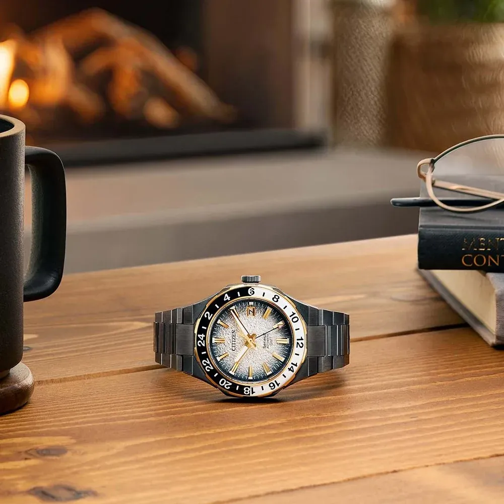 Reloj apoyado sobre una mesa de madera, fondo desenfocado con chimenea, libros y una taza