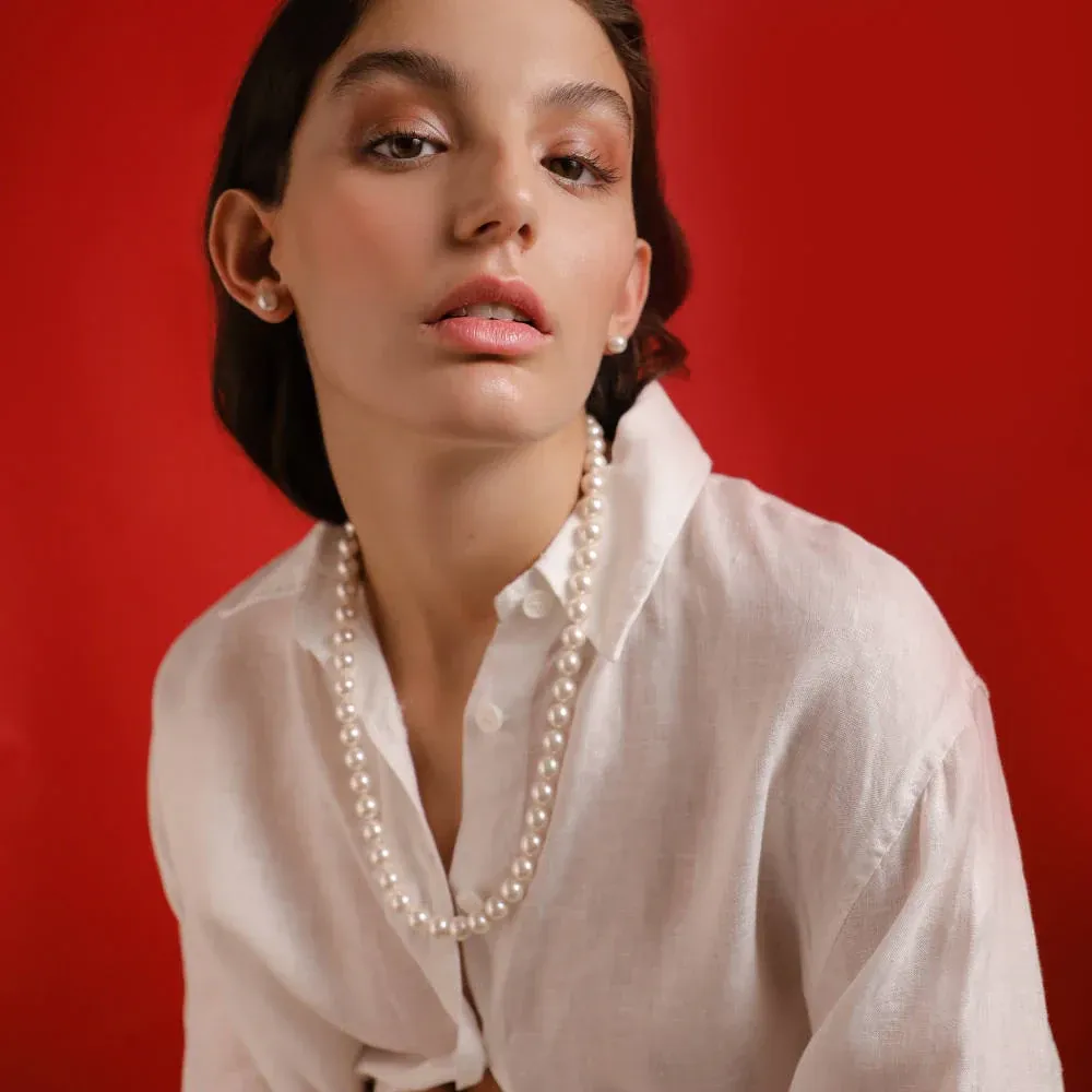 Pearl necklace on model wearing a white shirt, medium close-up shot, vibrant red background.