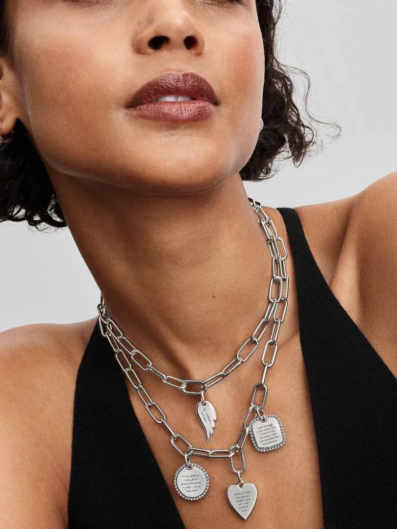 Close-up van twee zilveren schakelkettingen met gegraveerde hangers om de hals van een model.