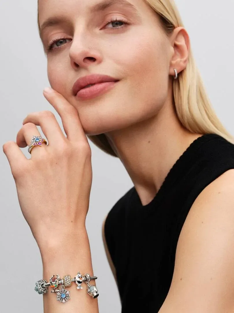 Primer plano de mano con anillo y pulsera de charms, modelo con fondo neutro claro.