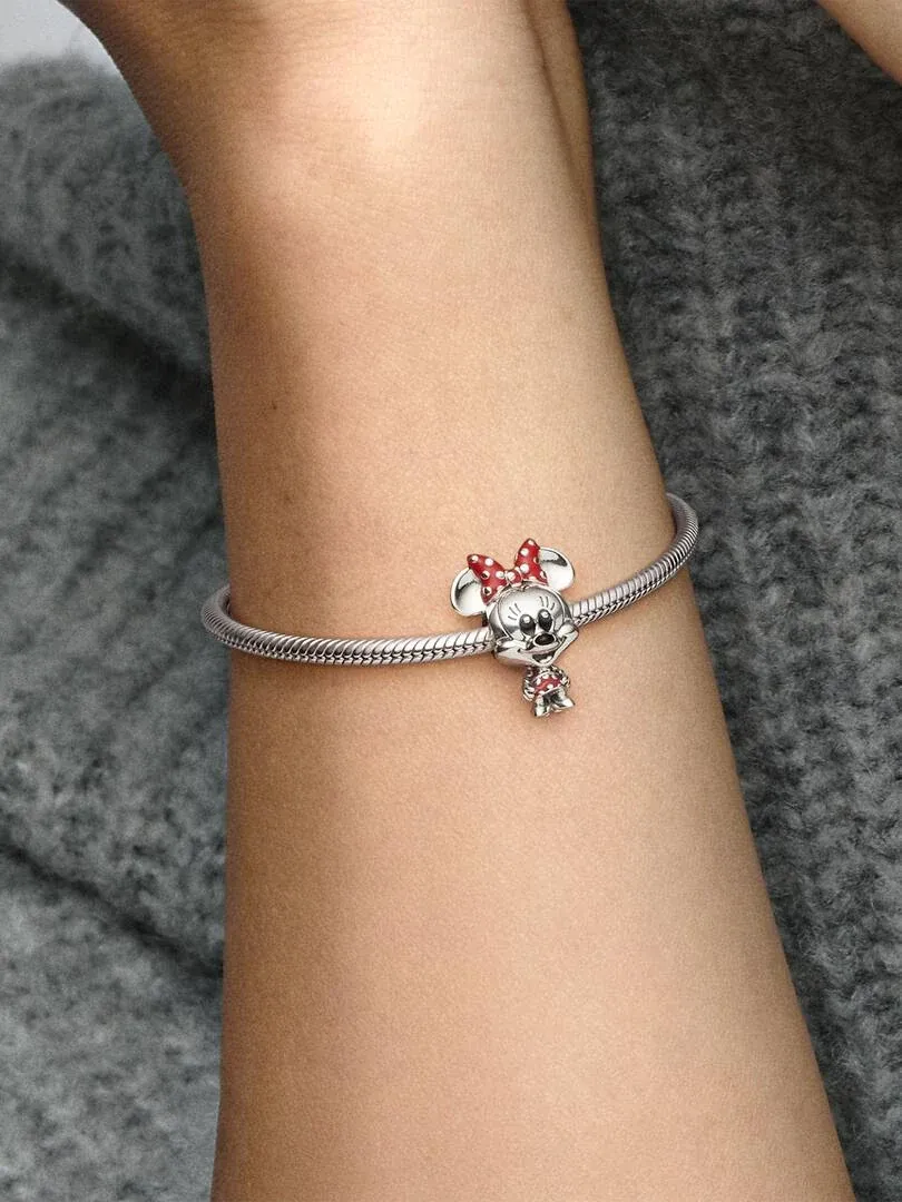 Charm de Minnie Mouse en brazalete de plata, toma lateral sobre muñeca con fondo gris texturizado.