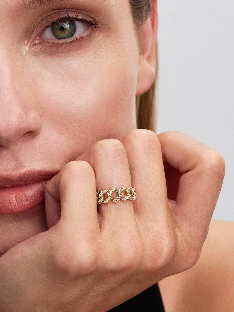 Primer plano del anillo de cadena cubana en el dedo, toma lateral con rostro de modelo desenfocado al fondo.