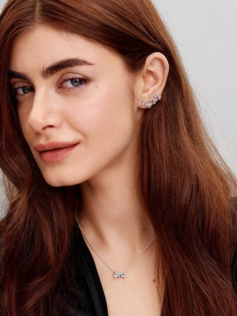 Gros plan d'un modèle portant des boucles d'oreilles nœud et un collier assorti, vue de face sur fond neutre.