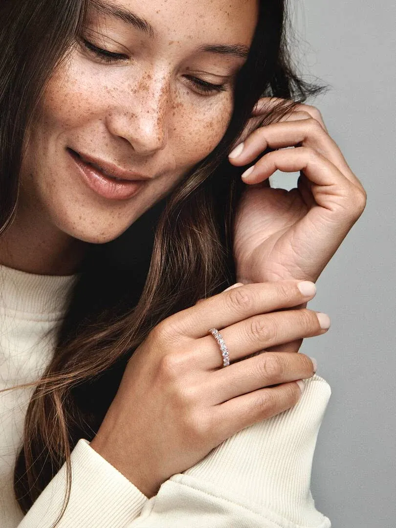 Primer plano de anillo con circonitas en dedo anular, modelo con pecas y fondo gris neutro.