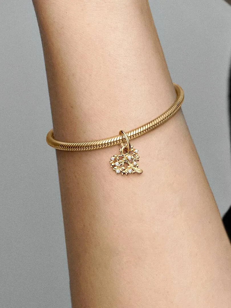 Primer plano de la pulsera de oro con colgante de árbol en forma de corazón sobre la muñeca, fondo neutro.