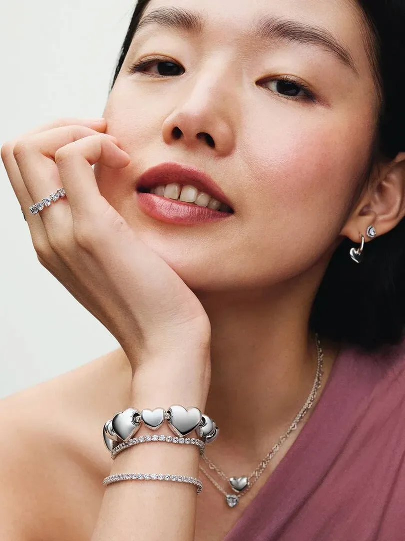 Close-up of model wearing silver rings, bracelets, and earrings against a neutral background.