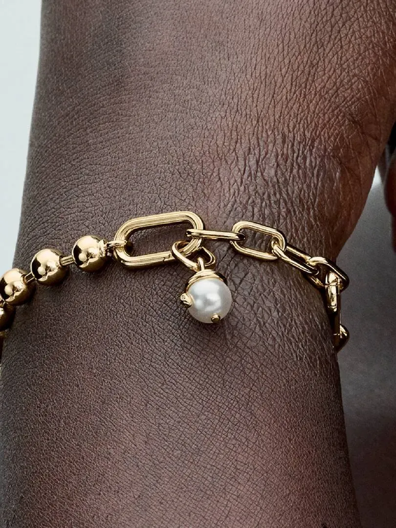 Close-up van de gouden armband met parelpendant op een pols, zijaanzicht.