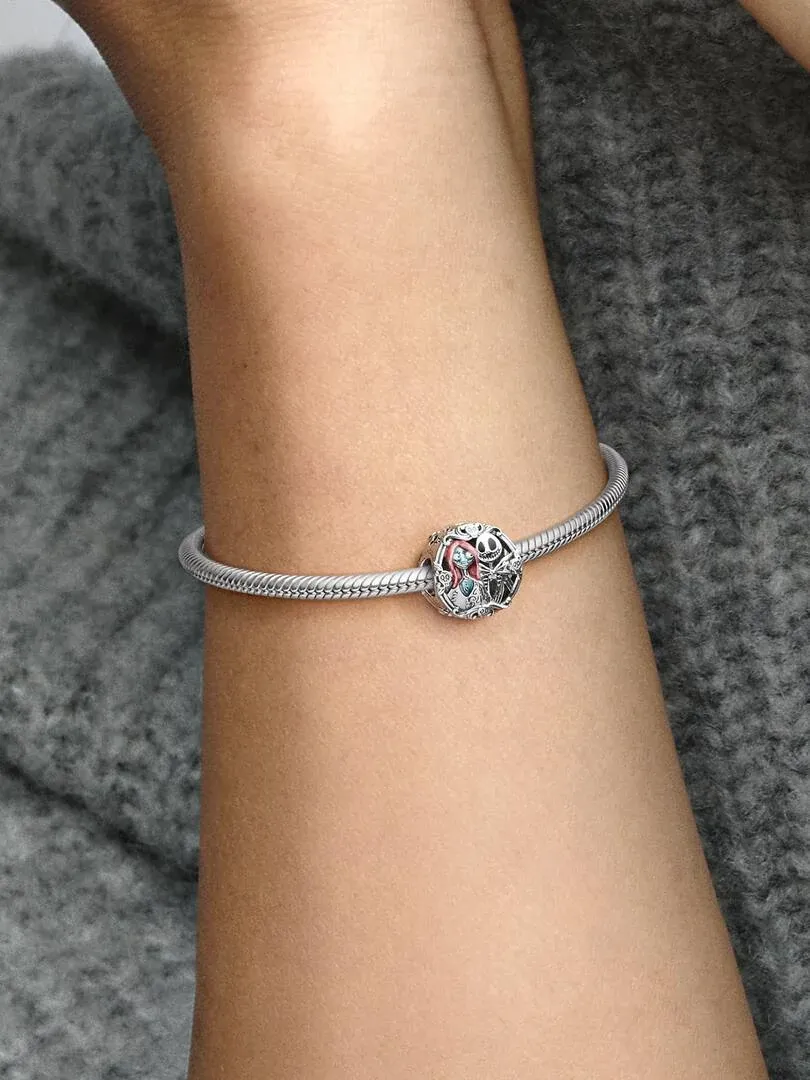 Nahaufnahme eines Silber-Charms an einem Armband, getragen am Handgelenk vor grauem strukturiertem Hintergrund.