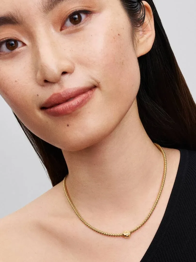 Close-up of gold charm necklace on a model's neck, front view against a neutral background.