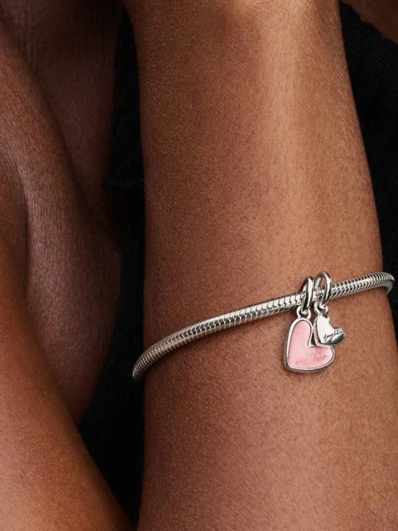 Primer plano del charm de corazón rosa en una pulsera de plata, sobre la muñeca con fondo oscuro.
