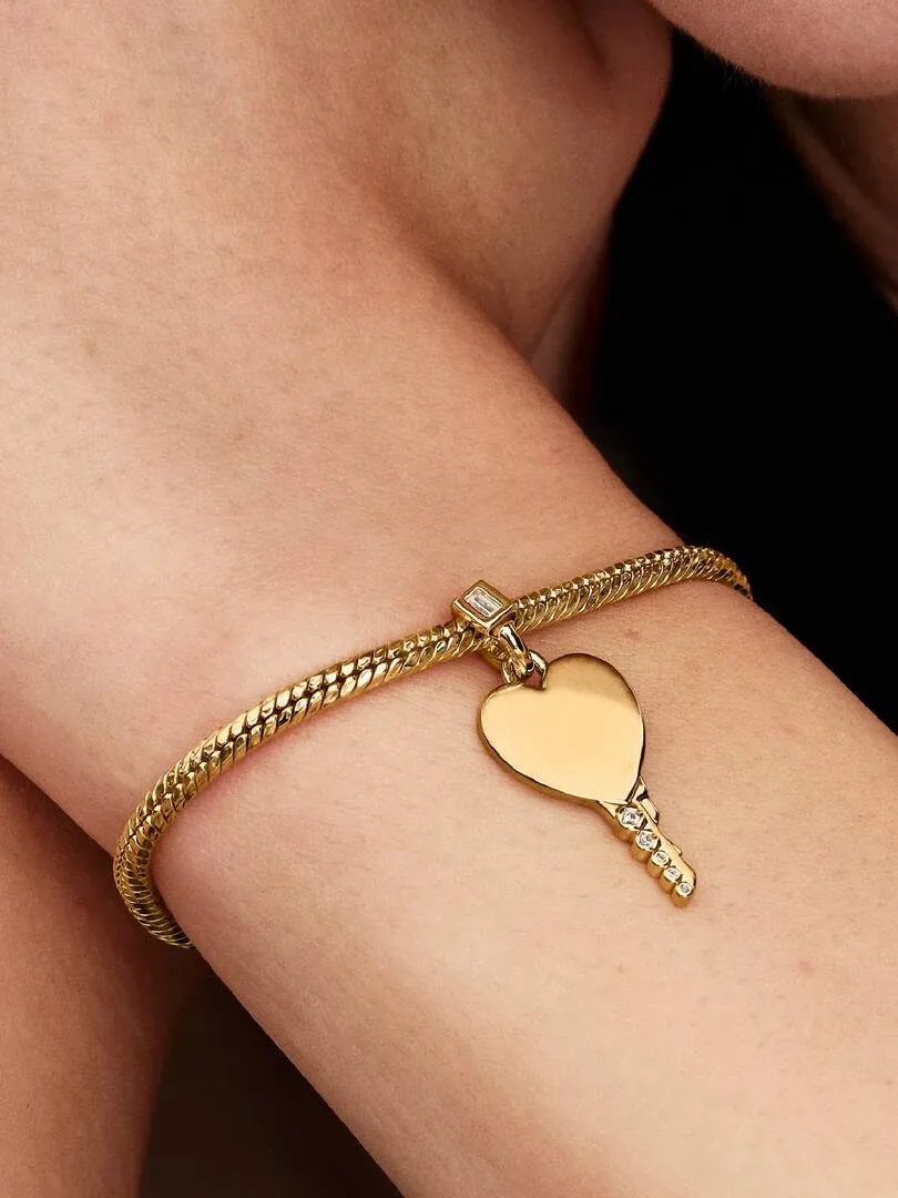 Primer plano del colgante de llave en forma de corazón sobre la muñeca, toma lateral con fondo oscuro.