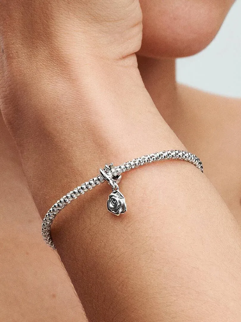 Primer plano de charm de rosa en pulsera de plata, puesto en la muñeca con fondo desenfocado.