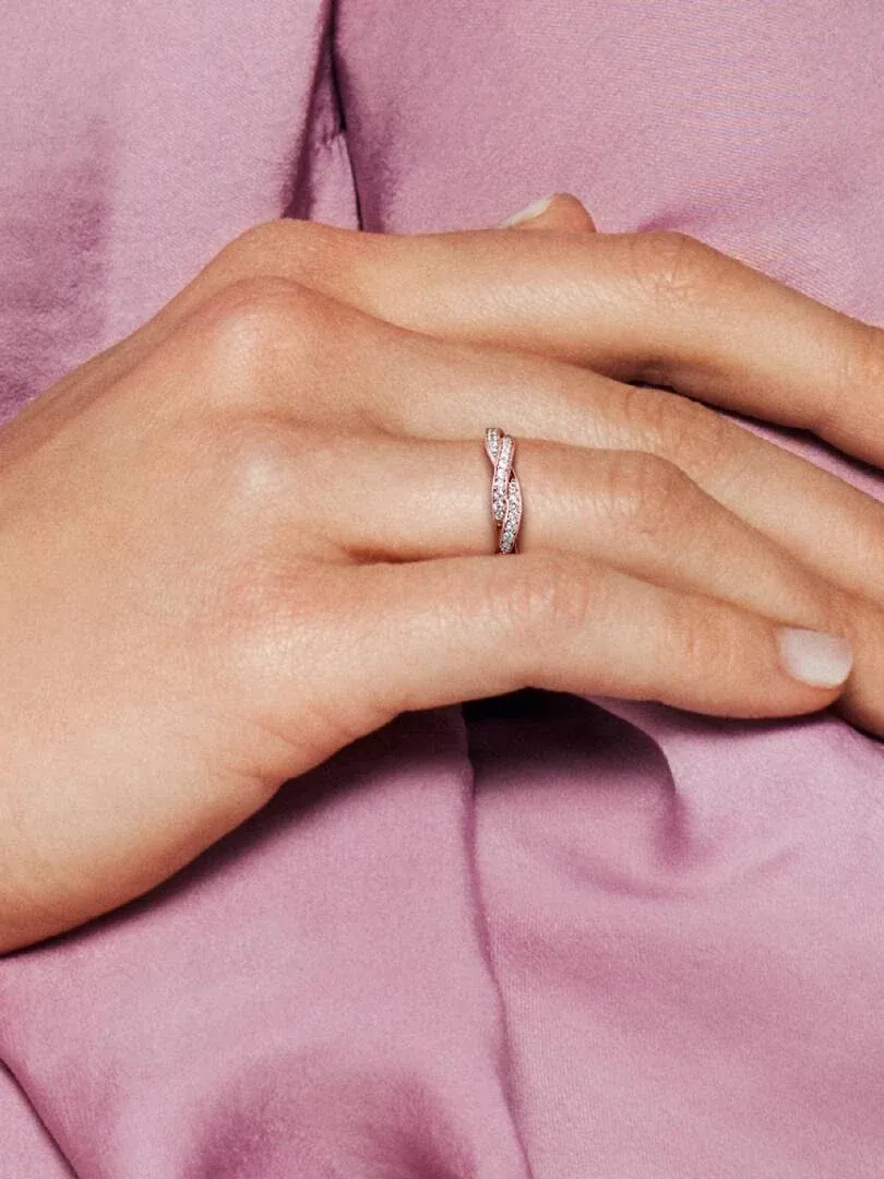 Primer plano del anillo de oro rosa en el dedo anular, toma lateral sobre fondo de tela rosa suave.