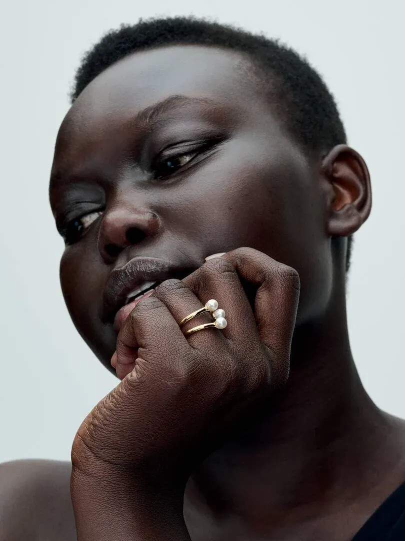 Primer plano del anillo de tres bandas con perlas blancas puesto en el dedo, sobre la mano de una modelo.