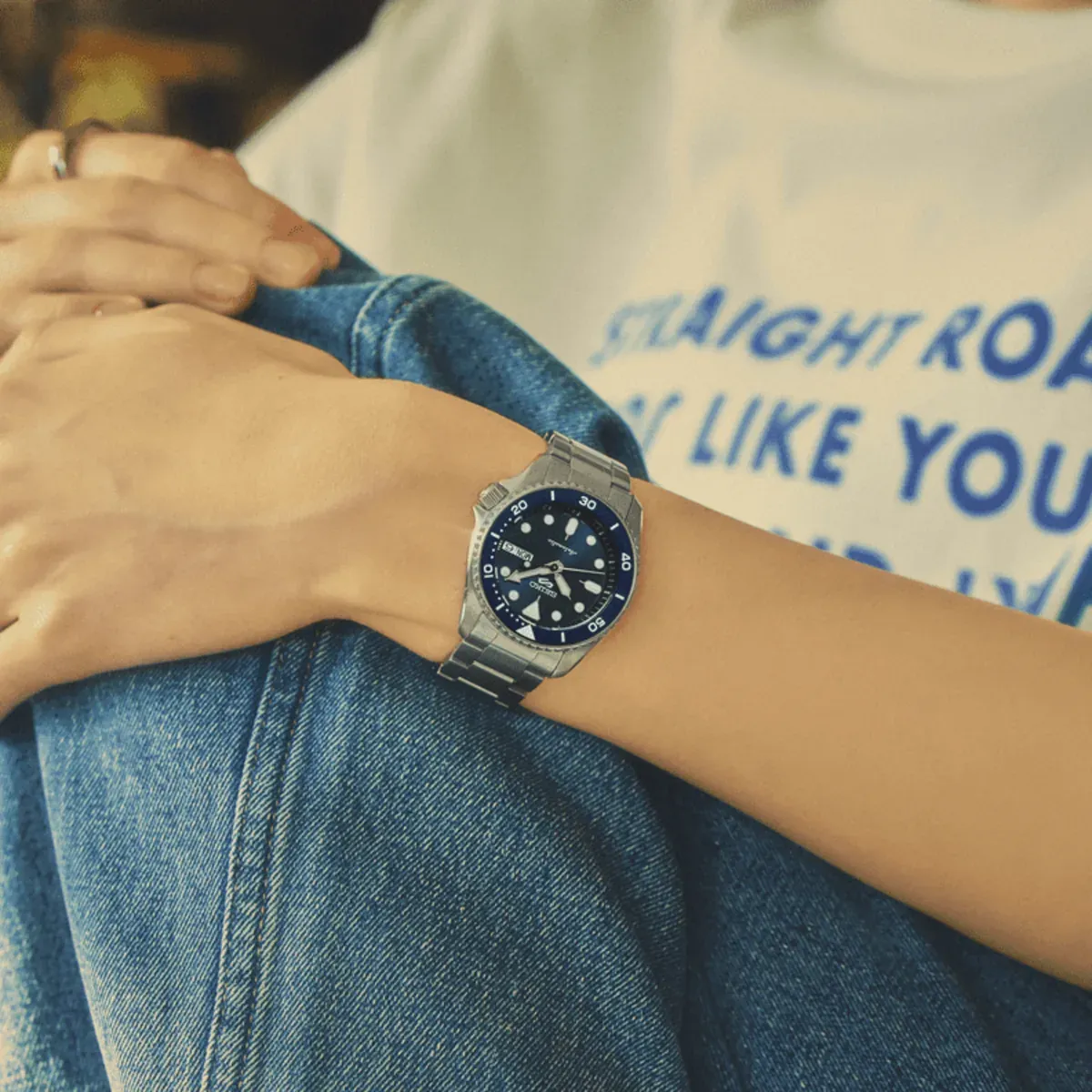 Reloj puesto en la muñeca de un modelo, vestido con camiseta blanca y vaqueros, toma en plano medio.