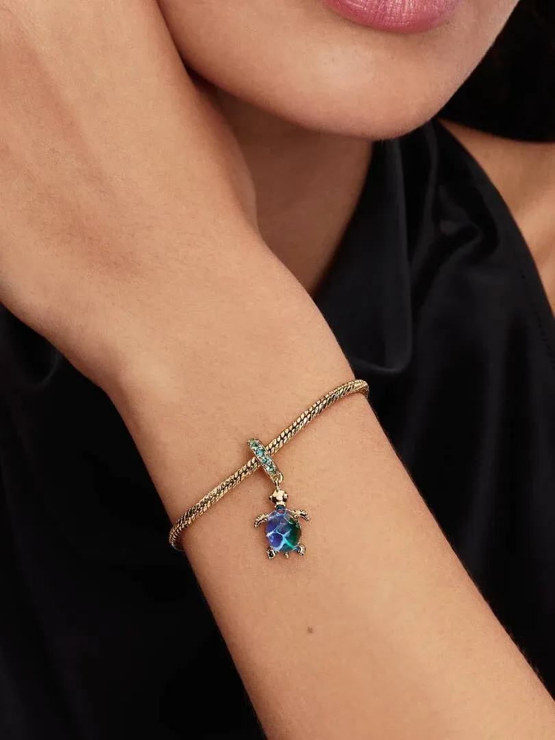 Gros plan du bracelet avec charm tortue sur un poignet, vue latérale sur fond sombre.