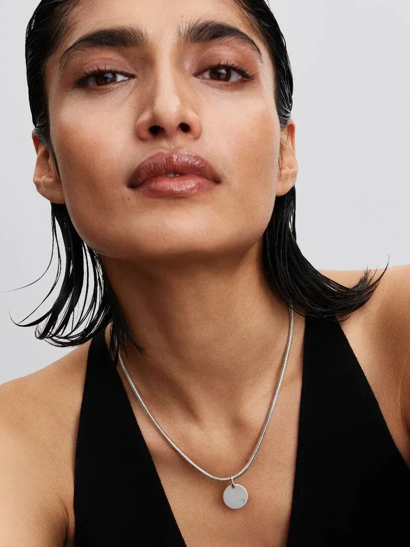 Gros plan du pendentif disque sur le cou d'un mannequin, vue de face sur fond neutre.