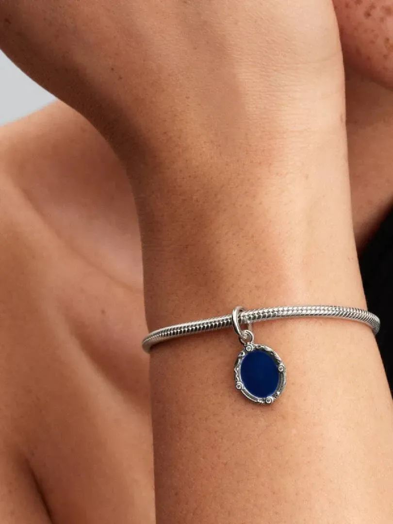 Primer plano del charm azul en una pulsera de plata, visto lateralmente sobre la muñeca.