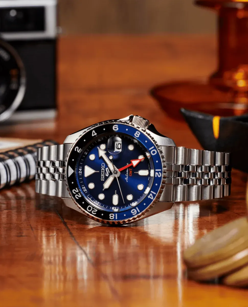 Reloj apoyado sobre superficie de madera, toma en ángulo bajo, fondo con objetos decorativos desenfocados
