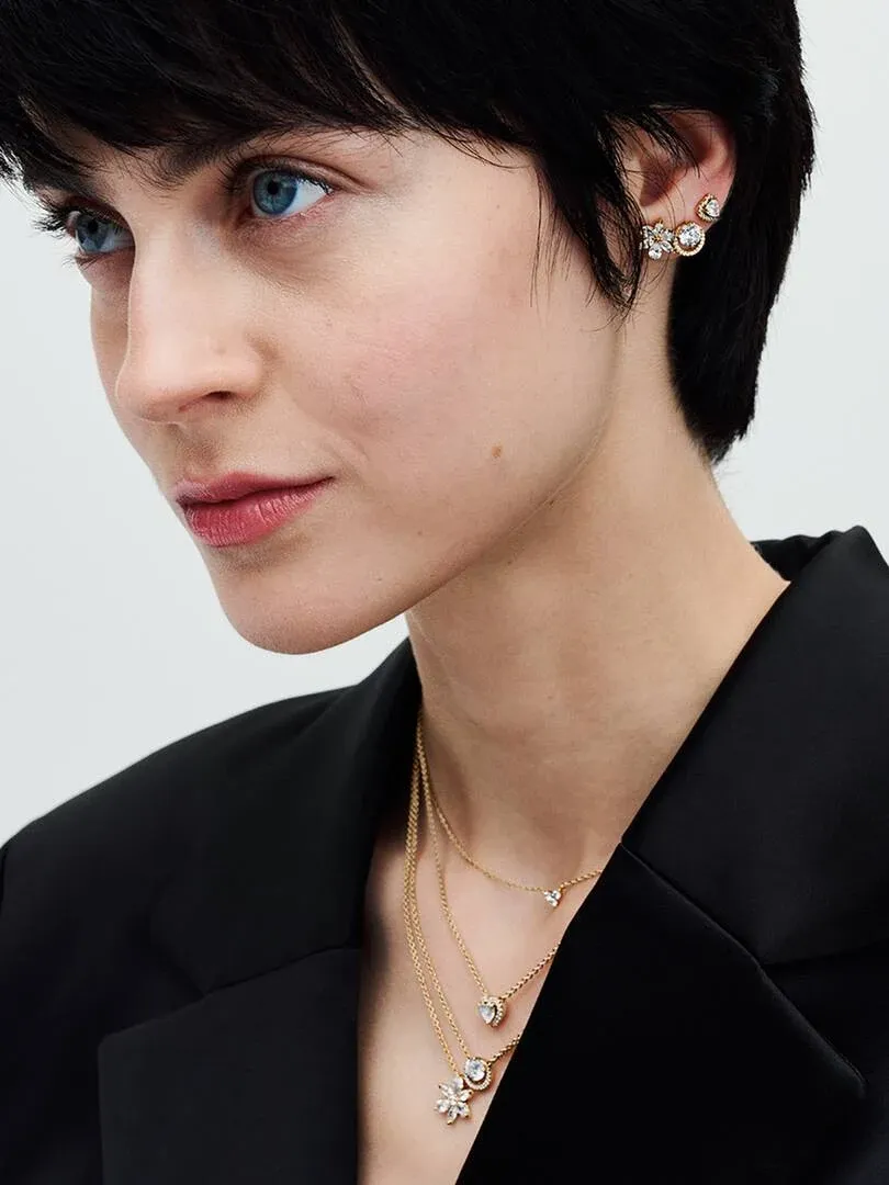 Gros plan de profil d'un modèle portant des colliers superposés et des boucles d'oreilles, fond neutre.