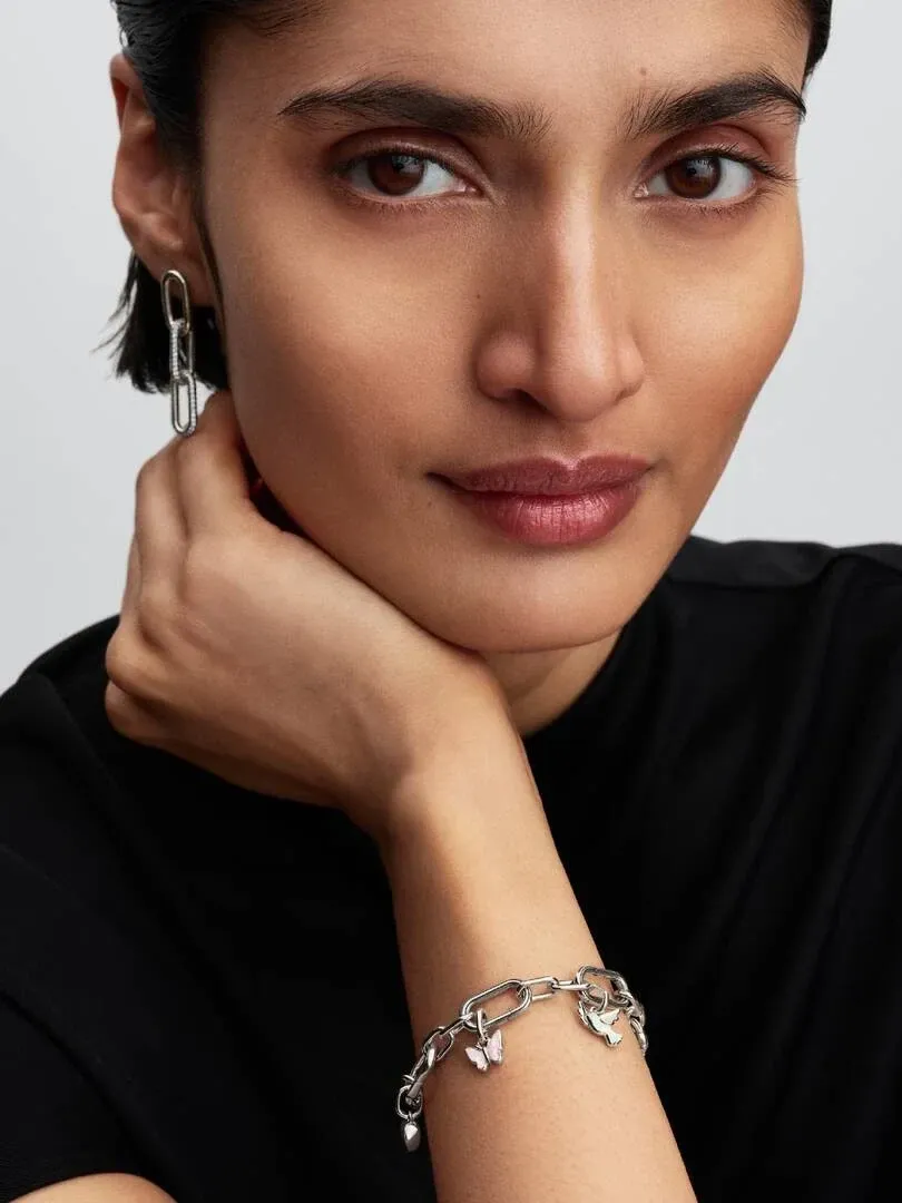 Nahaufnahme eines Models mit Creolen und Gliederarmband mit Charms, neutraler Hintergrund.