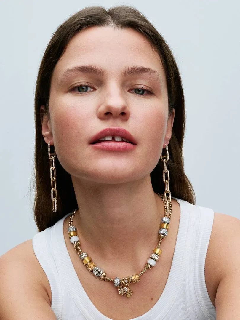 Gros plan d'un mannequin portant un collier et des boucles d'oreilles à maillons dorés, vue de face.