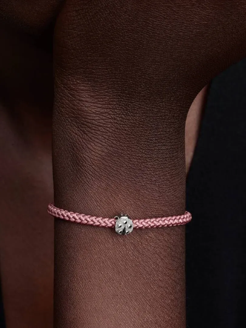Close-up van een lieveheersbeestje charm aan een roze armband, gedragen om de pols.