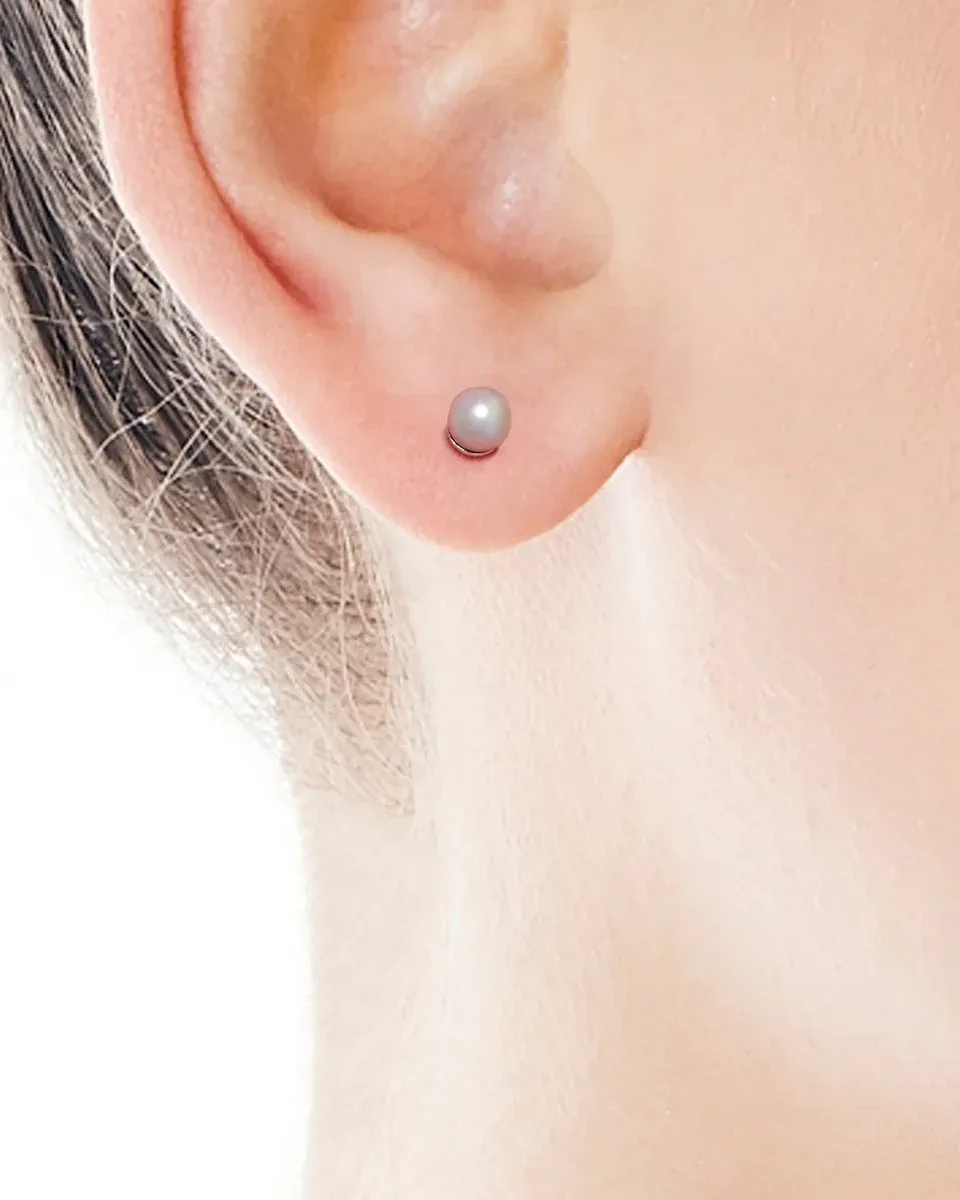 Close-up side view of a pearl stud earring worn on the earlobe, light neutral background.