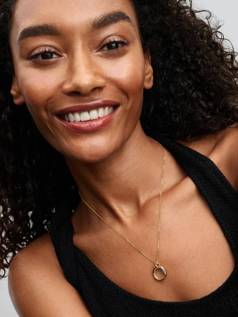Close-up of the necklace with a circular pendant on a model's neck, blurred neutral background.