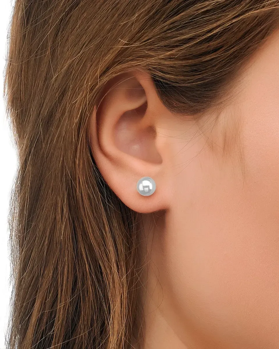 Close-up side view of a white pearl stud worn on the earlobe, blurred background.