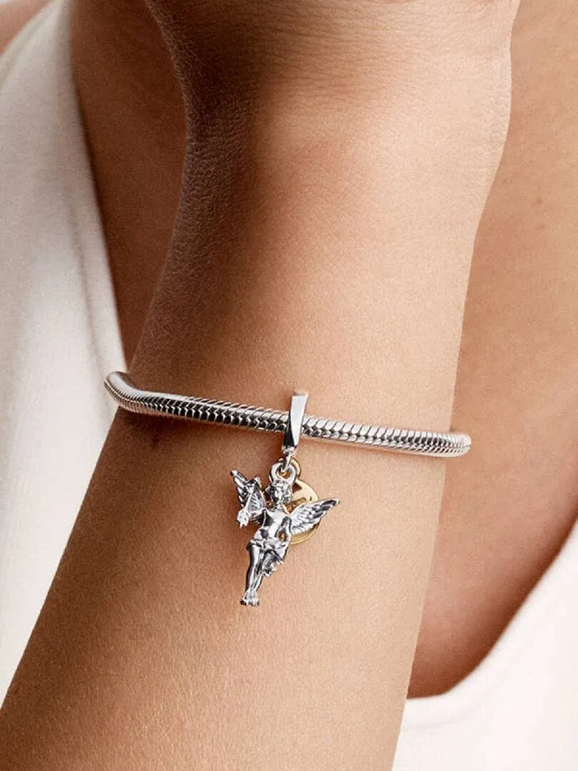 Primer plano del charm de Cupido colgado en una pulsera de plata, puesto en la muñeca.