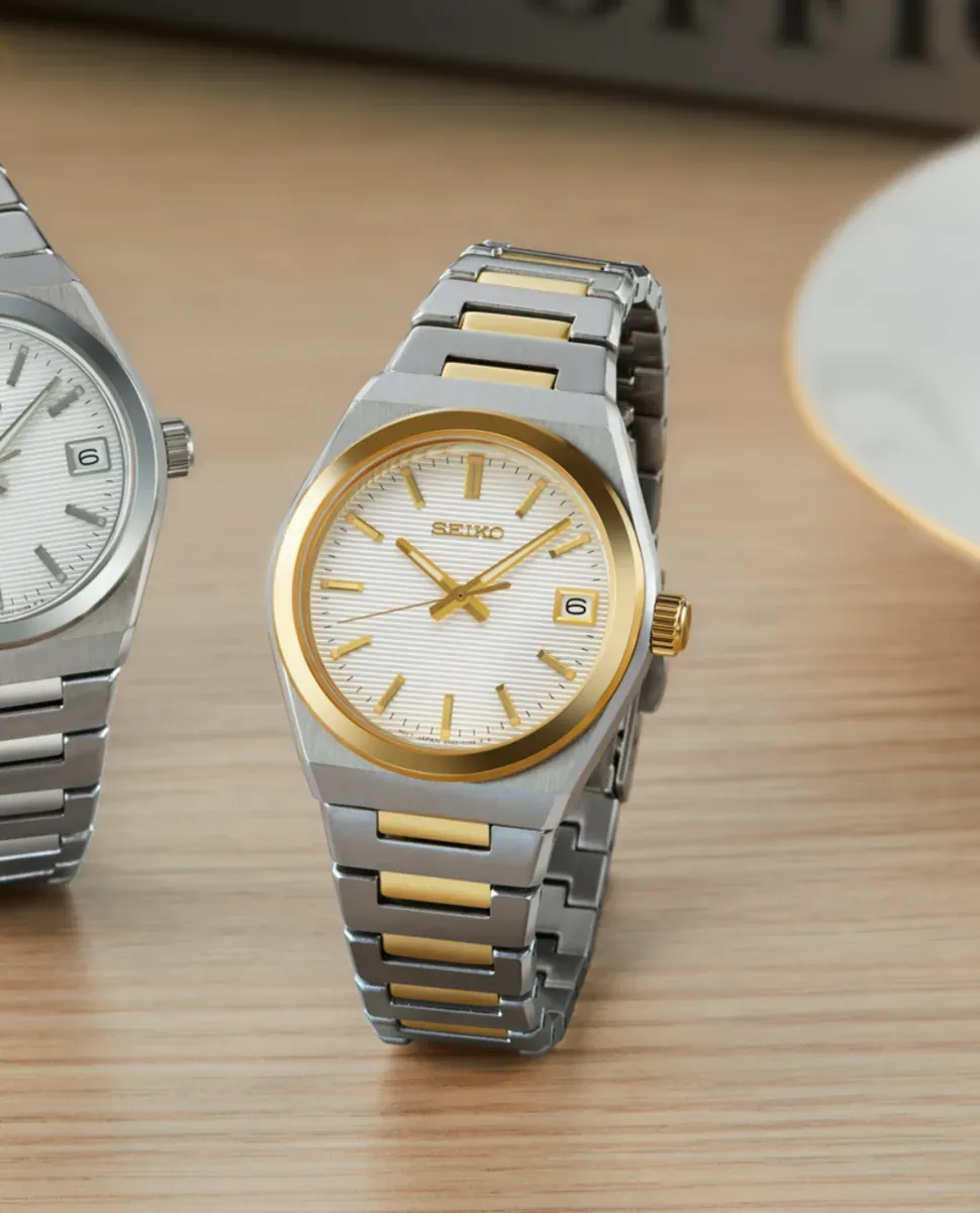 Reloj posicionado verticalmente sobre superficie de madera clara, composición con segundo reloj, fondo desenfocado.