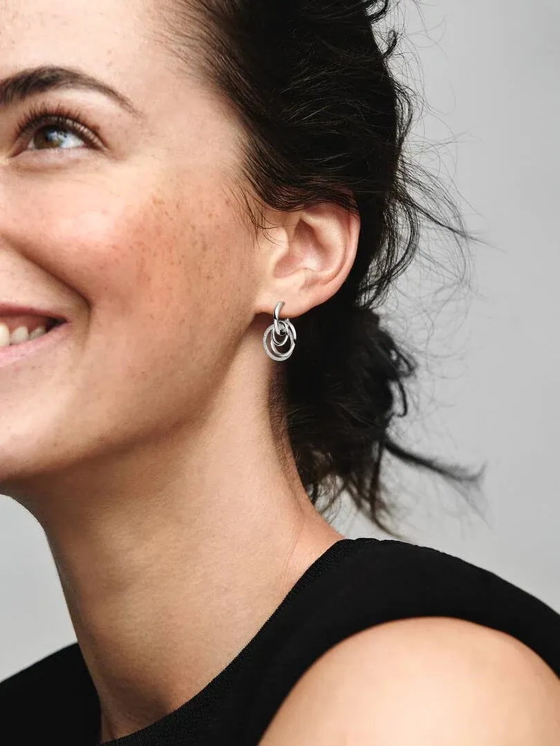 Close-up van verstrengelde oorring gedragen aan het oor, zijaanzicht op model met grijze achtergrond.