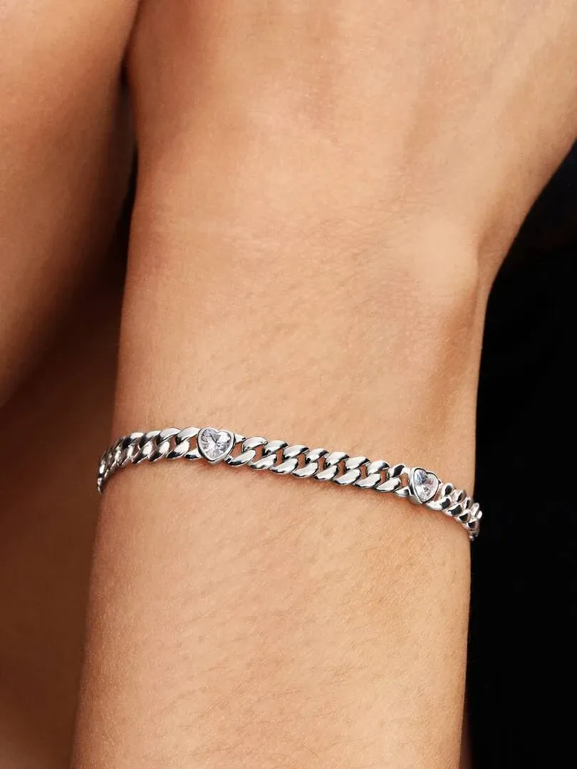 Primer plano de la pulsera de cadena cubana con detalles de corazón sobre la muñeca, toma lateral.