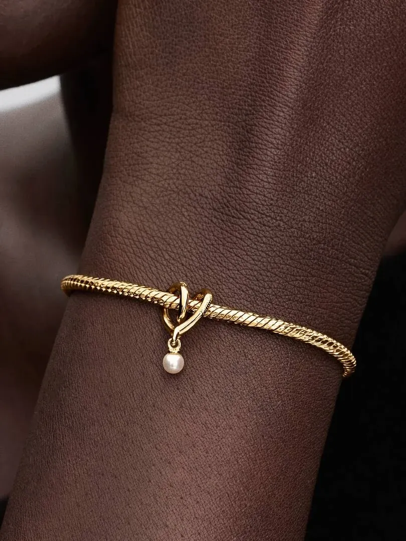 Gros plan du charm cœur avec perle blanche sur un poignet, vue de profil en contre-plongée.