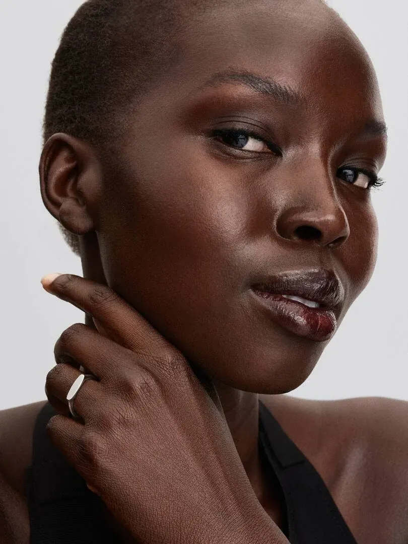 Close-up of a hand resting on the neck, showing the silver bar ring on dark skin.