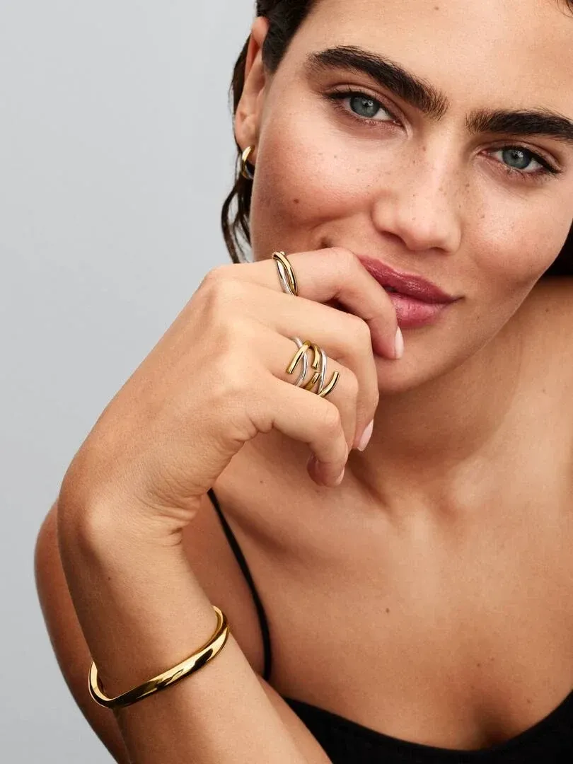 Primer plano de mano femenina con anillo de dos tonos, modelo apoyando la barbilla, fondo neutro.