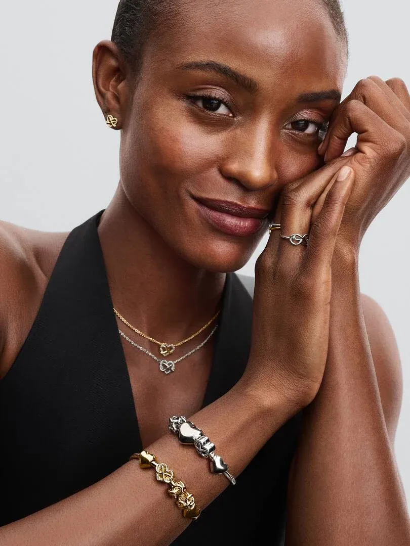 Modèle portant un bracelet, un collier et une bague, plan moyen de face sur fond gris clair.