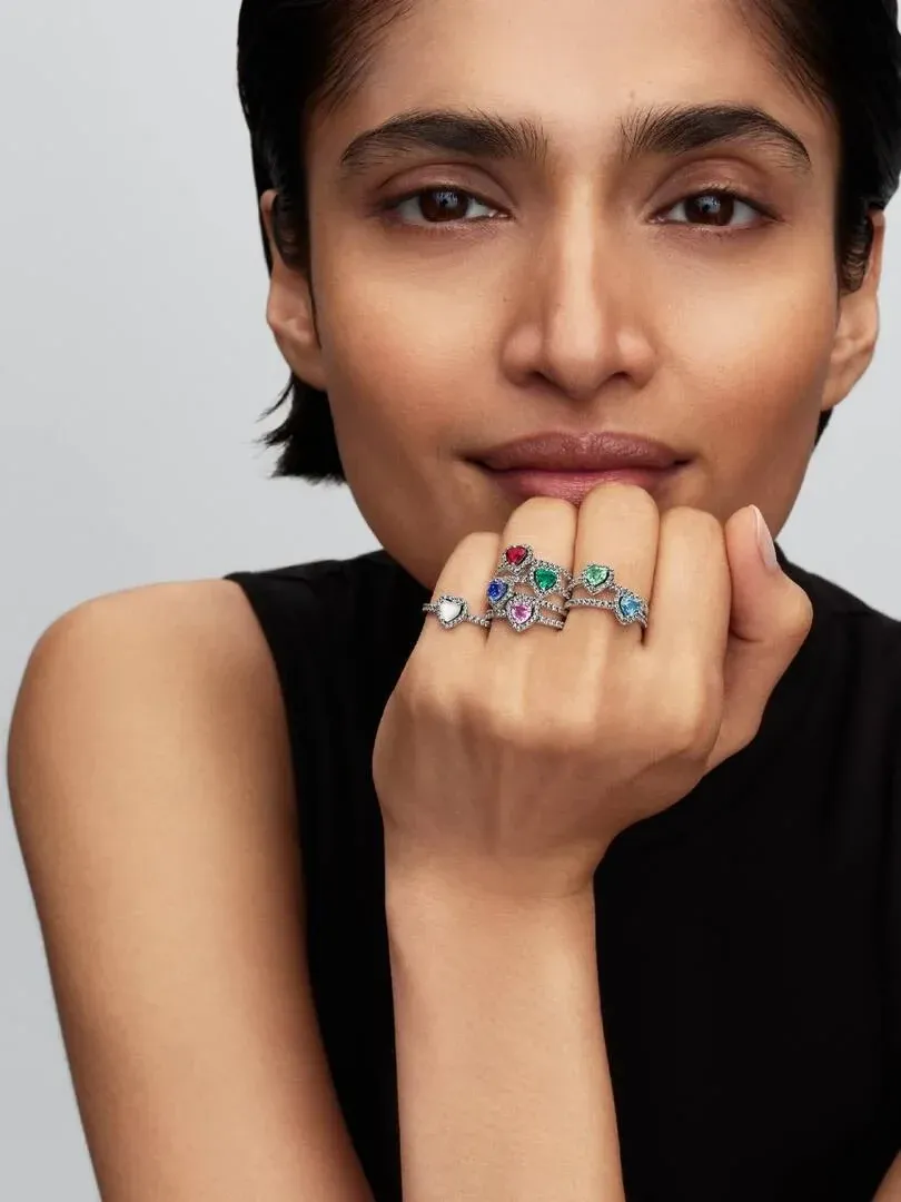 Close-up of hand wearing three heart rings resting on chin, front view with neutral background.