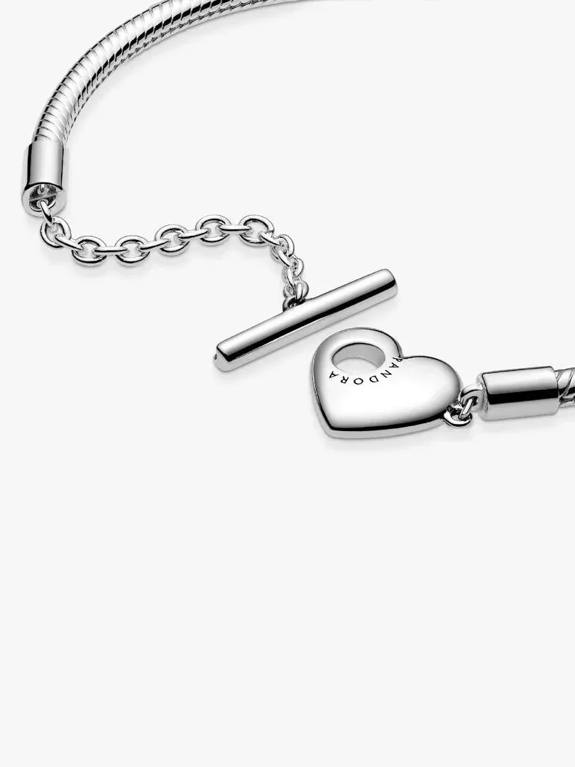 Primer plano del cierre de barra en T y el dije de corazón, sobre fondo blanco.