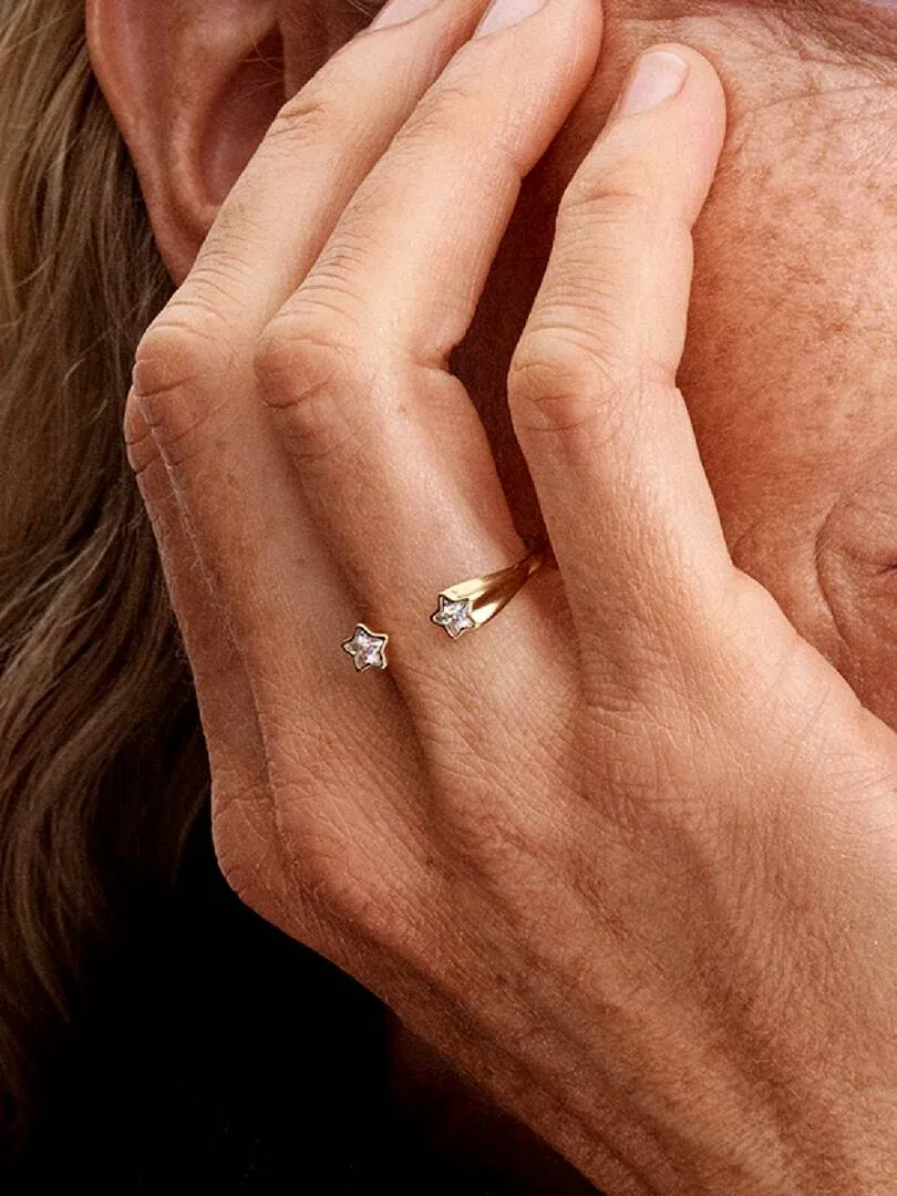 Primer plano de anillo abierto con estrellas sobre dedo, toma lateral en mano con piel pecosa.
