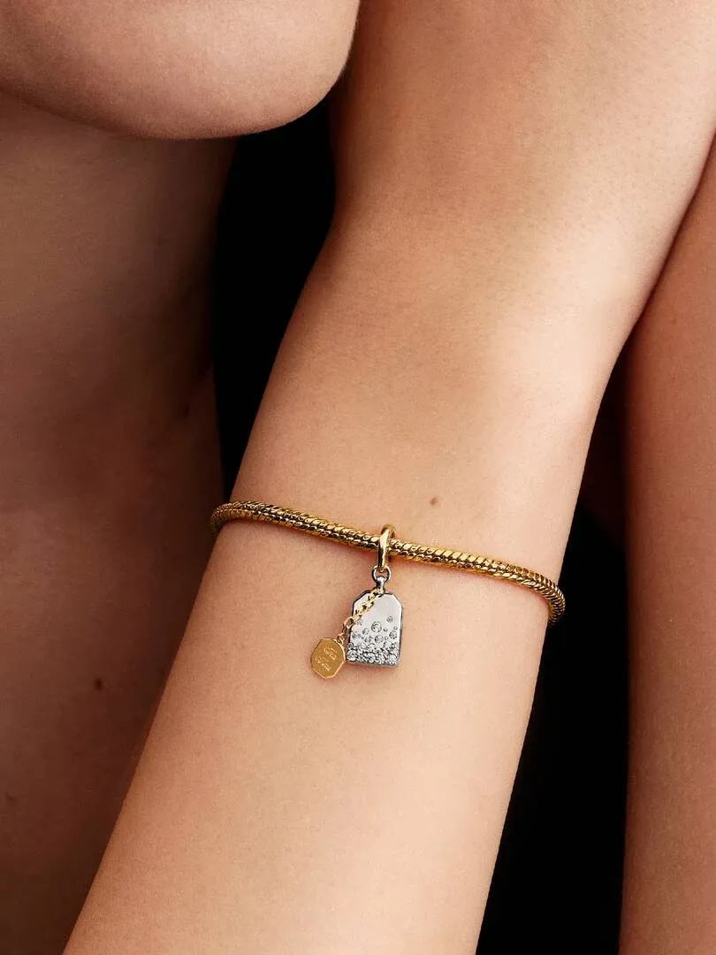 Primer plano del colgante de bolsa de té en una muñeca, toma lateral con fondo oscuro desenfocado.