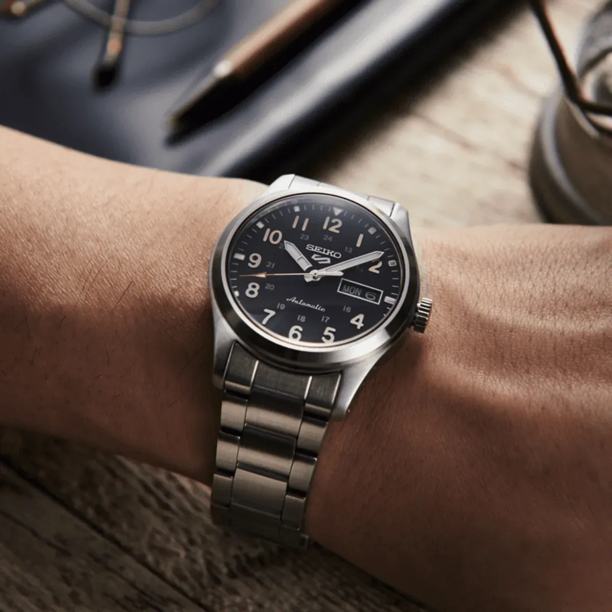 Reloj puesto en muñeca, toma en ángulo con fondo desenfocado en tonos neutros.