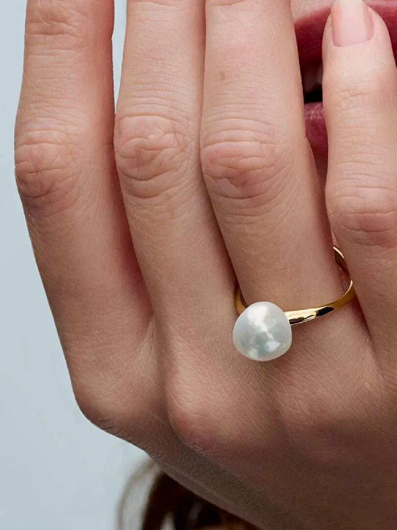 Primer plano lateral de anillo con perla barroca en dedo, fondo desenfocado.