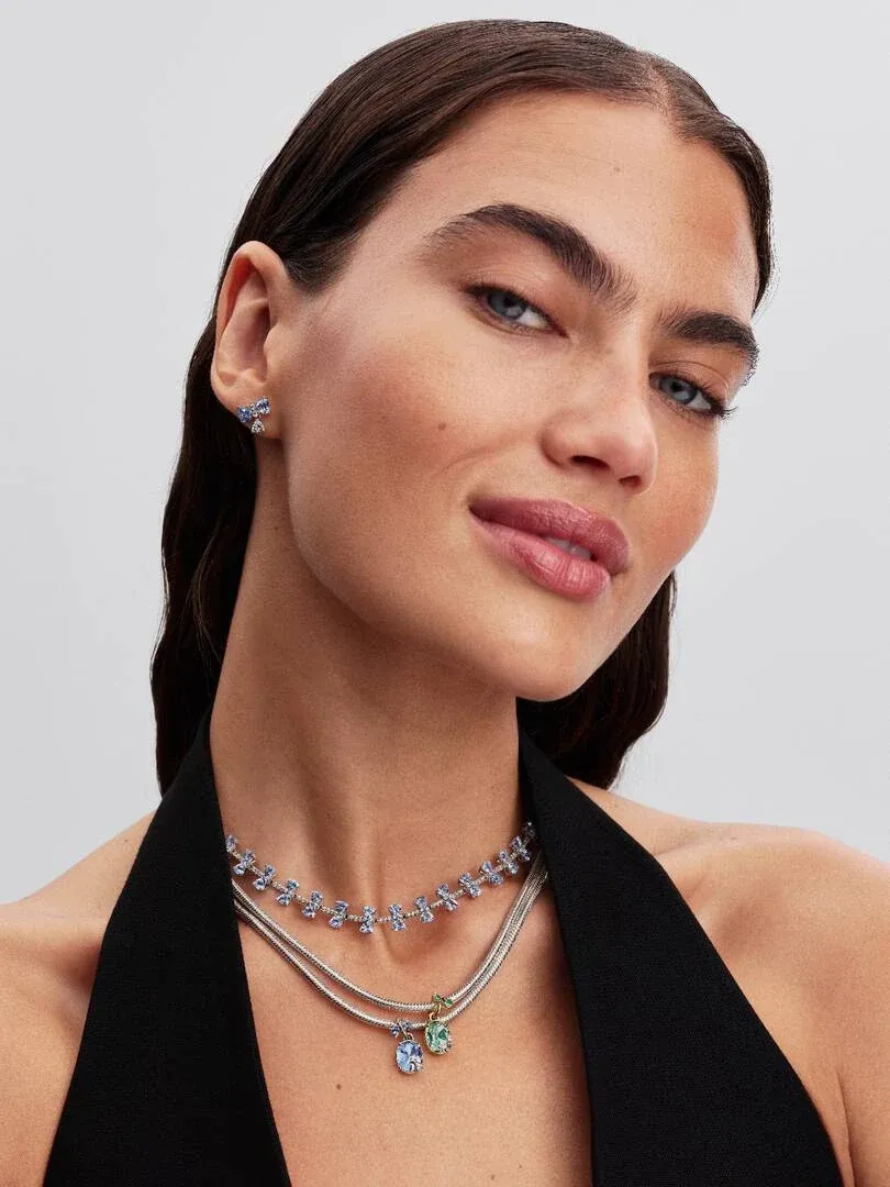 Gros plan d'un modèle portant des puces d'oreilles nœud bleu et un collier, vue de face sur fond neutre.