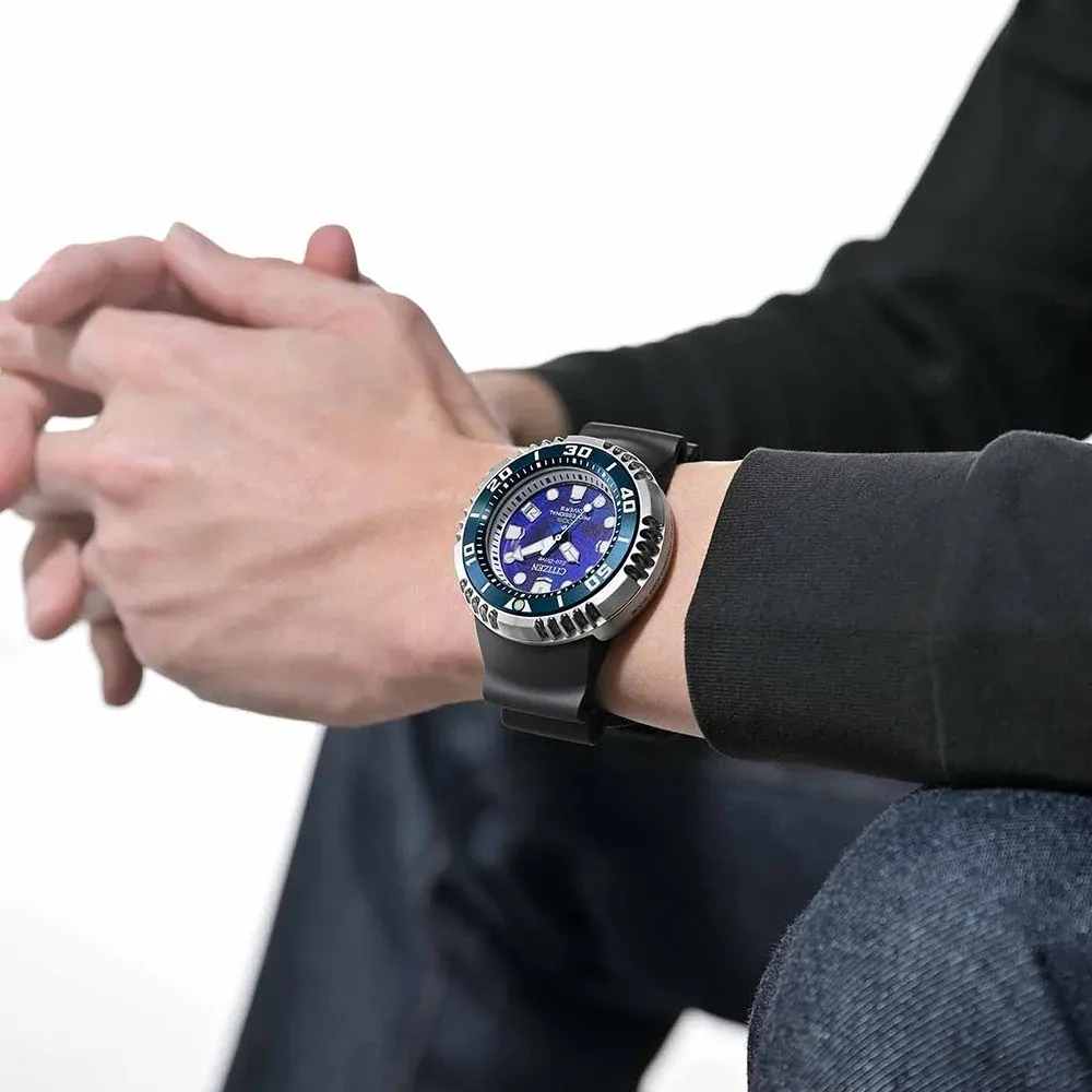 Hombre con reloj puesto en la muñeca, manos entrelazadas, viste camisa negra y vaqueros, fondo blanco