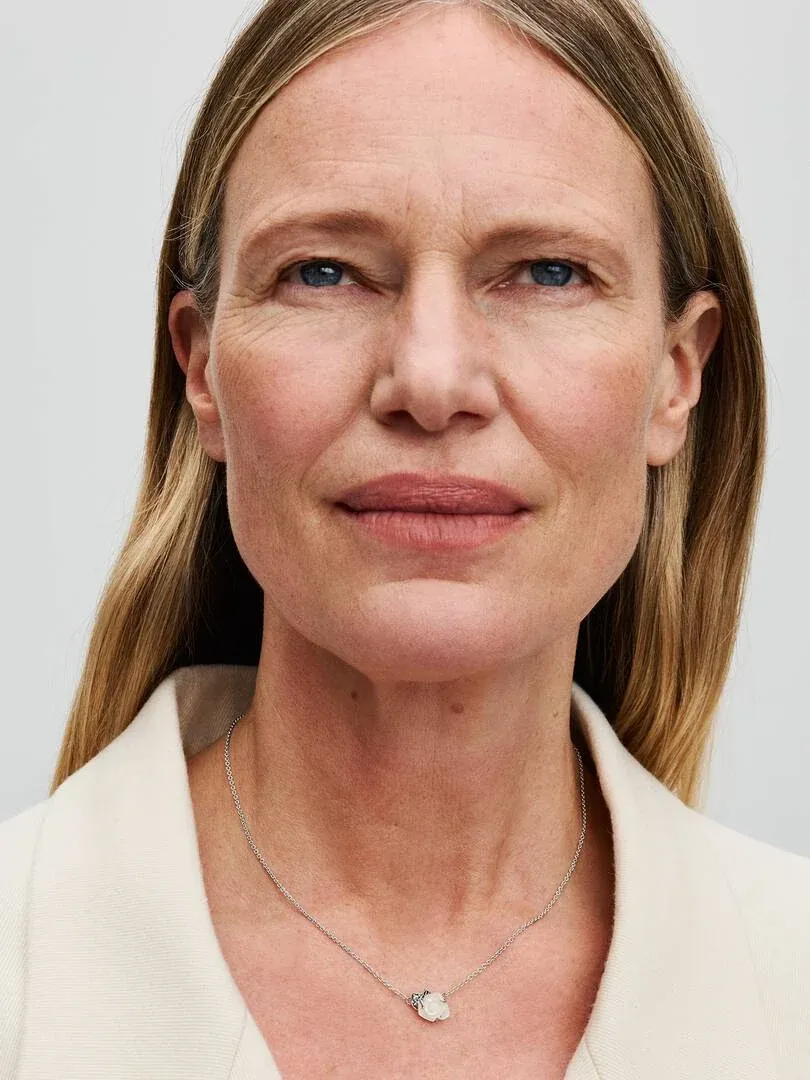 Primer plano del colgante de rosa blanca sobre el cuello de una modelo, toma frontal con fondo neutro.